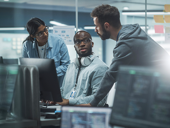 Three people in lab coats discussing something near a computer.