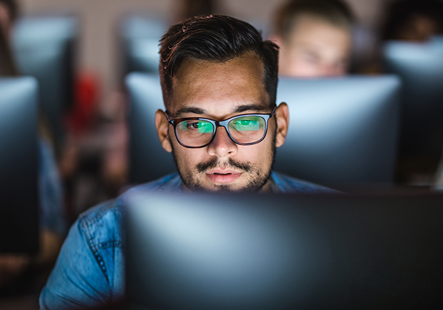 A male wearing glasses on the computer facing the camera.